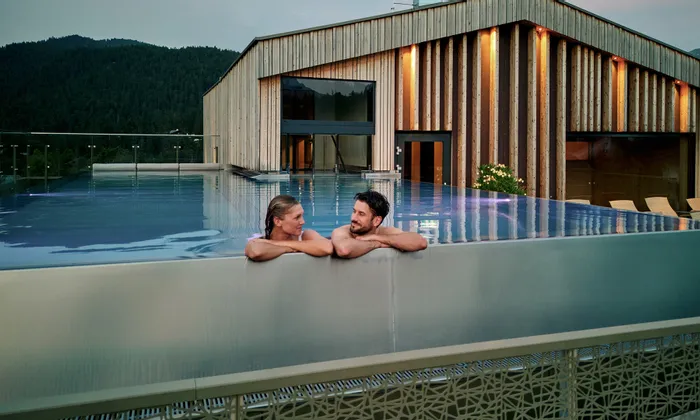 Paar entspannt im Infinity-Pool auf dem Dach eines luxuriösen Alpinresorts mit Holzarchitektur
